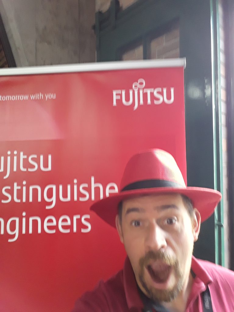 Jon in a Red Hat from RedHat standing in front of the Fujitsu Distinguished Engineers banner