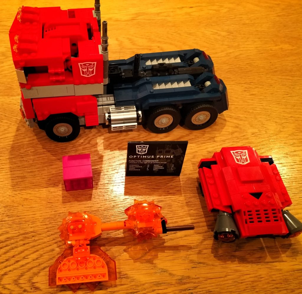 LEGO Optimus Prime set 10302 in vehicle mode, with the axe, jetpack and Energon cube on the table alongside the informational plaque.