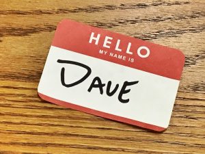 A red and white label on a wooden surface. The label reads "Hello my name is Dave"