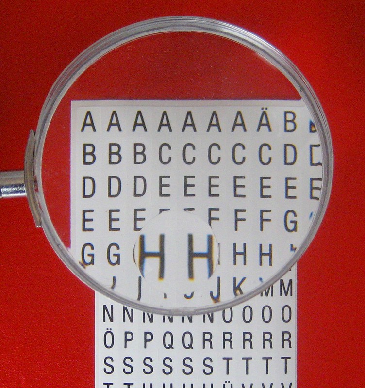 A magnifying glass focused on the letter H looking at a page of letters in alphabetical order, with a red background